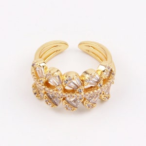 Könnte beinhalten: Ein goldener Ring mit einem filigranen Design, das aus einer Reihe von miteinander verbundenen, klaren, baguetteförmigen Steinen besteht.