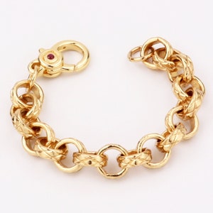 May include: A gold chain bracelet with a textured design. The bracelet has a clasp with a small red stone.