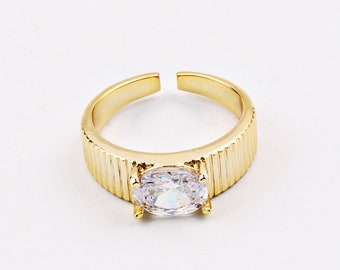 May include: A gold ring with a large, clear, oval-shaped gemstone. The band of the ring has a ridged texture.