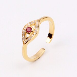 May include: Gold adjustable ring with a red and white evil eye design. The ring is set with small clear stones.