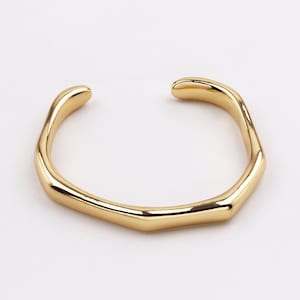 May include: A gold-toned, open-ended ring with a unique, irregular shape. The ring is made of metal and has a smooth, polished finish.