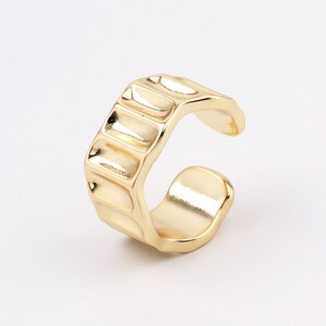 May include: Gold ear cuff with a textured design. The cuff is open and can be adjusted to fit different ear sizes.