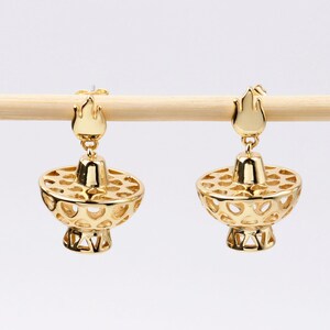 May include: A pair of gold-tone earrings with a delicate, openwork design. Each earring features a small, flame-shaped top and a larger, round, openwork bottom.