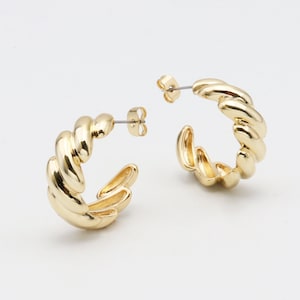 May include: A pair of gold-toned hoop earrings with a twisted design. The earrings are made of metal and have a polished finish.