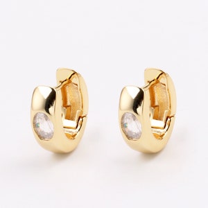 Könnte beinhalten: Ein Paar goldene Creolen mit einem kleinen, klaren Stein, der in jeden Reifen eingefasst ist.