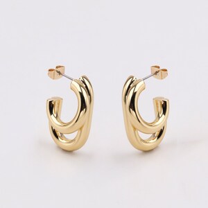 May include: A pair of gold-toned hoop earrings with a double-loop design. The earrings are made of metal and have a polished finish.