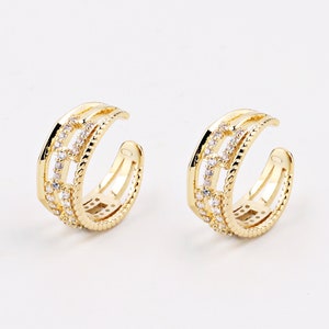 May include: A pair of gold ear cuffs with a triple band design and clear cubic zirconia stones.