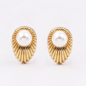 May include: A pair of gold-tone earrings with a pearl in the centre of each earring. The earrings have a scalloped design.