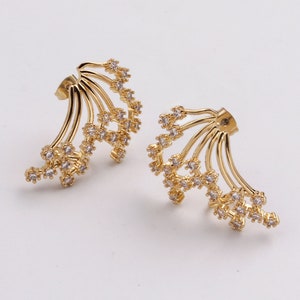 Puede incluir: Un par de pendientes de oro con un diseño delicado y curvo. Cada pendiente presenta múltiples hebras adornadas con pequeñas piedras de circonita cúbica transparentes.