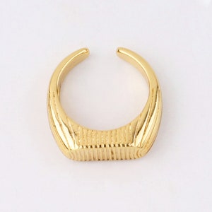May include: A gold-toned ring with a textured, rectangular band. The ring is open and has a simple, minimalist design.