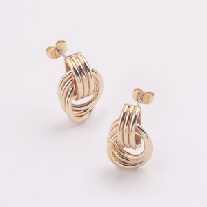 May include: A pair of gold knot-shaped earrings. The earrings are made of a thick, twisted metal and have a simple post back.