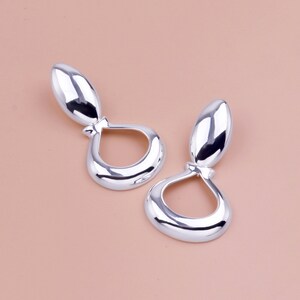 以下が含まれることがあります： 涙の形をしたシルバーのドロップイヤリングのペア。イヤリングは滑らかで磨かれた仕上げです。