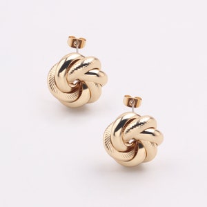 May include: A pair of gold knot-shaped earrings. The earrings are made of a smooth, shiny metal and have a simple, elegant design.