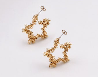 May include: A pair of gold star-shaped hoop earrings. The earrings are made of thin, twisted wire and have a delicate, intricate design.