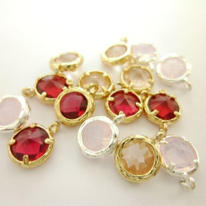 Op de afbeelding: Assortiment van gouden en zilveren bedelarmen met verschillende gekleurde glazen stenen. De stenen omvatten roze, rood en helder. De bedels zijn perfect voor het maken van sieraden of om een ​​toets van glans toe te voegen aan ambachten.