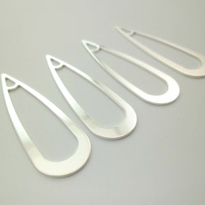 May include: Four silver teardrop-shaped earring blanks with a hole at the top.