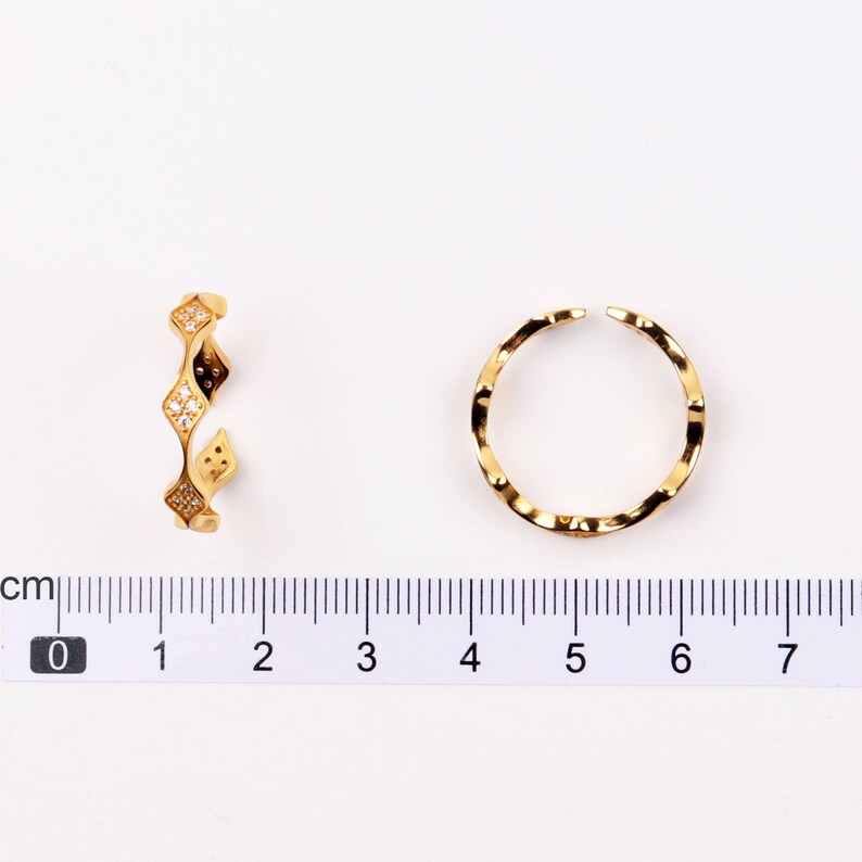 Puede incluir: Dos anillos de oro con un dise&ntilde;o texturizado. Un anillo tiene un dise&ntilde;o ondulado y el otro tiene un dise&ntilde;o en forma de diamante con piedras transparentes.