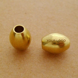 May include: Two gold oval-shaped beads. One bead has the text "YOUR LOGO" engraved on it.