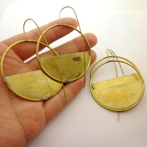 Pode incluir: Um par de brincos de latão dourado com um design de meio círculo. Os brincos são feitos de fio fino e têm um estilo simples e moderno.