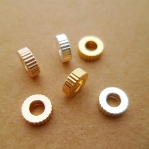 May include: Six metal spacer beads in gold, silver, and rose gold. The beads have a ridged design and a round hole in the center.