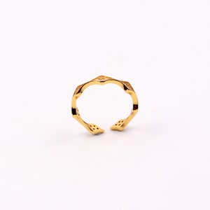 Puede incluir: Un anillo de oro con un dise&ntilde;o geom&eacute;trico y peque&ntilde;as piedras transparentes. El anillo es abierto y ajustable.
