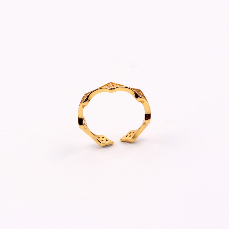 Puede incluir: Un anillo de oro con un dise&ntilde;o geom&eacute;trico y peque&ntilde;as piedras transparentes. El anillo es abierto y ajustable.