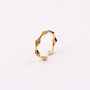 Puede incluir: Un anillo de oro con un dise&ntilde;o &uacute;nico y ondulado. El anillo est&aacute; adornado con peque&ntilde;as piedras transparentes.