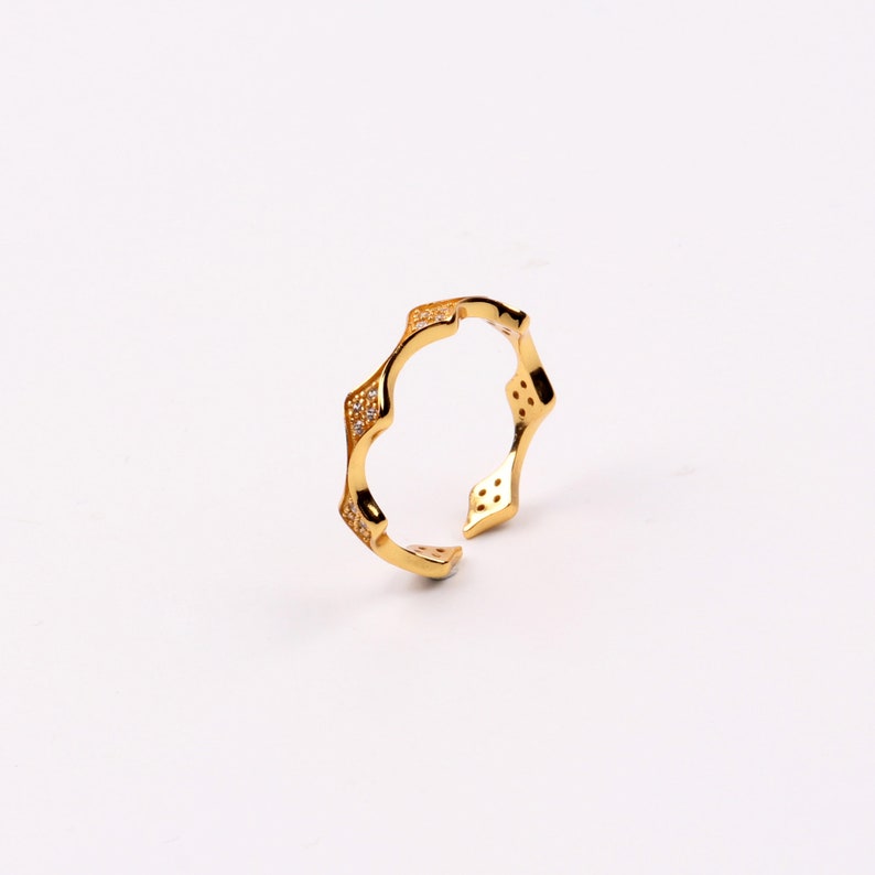 Puede incluir: Un anillo de oro con un dise&ntilde;o &uacute;nico y ondulado. El anillo est&aacute; adornado con peque&ntilde;as piedras transparentes.