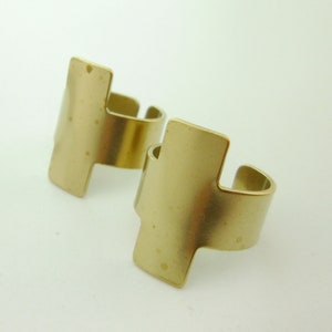 May include: Two gold-toned metal rings with a rectangular design. The rings are simple and minimalist, with a smooth, slightly textured finish.