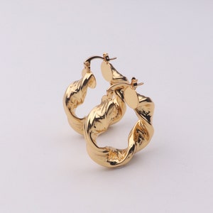 Puede incluir: Un par de pendientes de aro dorados con un diseño trenzado.