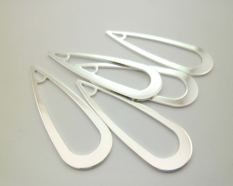 May include: Five silver metal teardrop-shaped earring blanks with a rounded edge and a hole at the top.