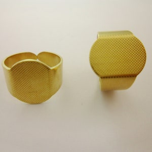 May include: Two gold-coloured metal rings with a round, textured surface. The rings are adjustable and can be worn on any finger.