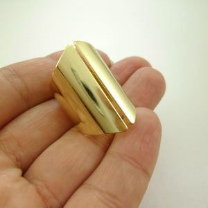 Puede incluir: Un anillo de metal de color dorado con un diseño único. El anillo está abierto por un lado y tiene una banda recta y plana.