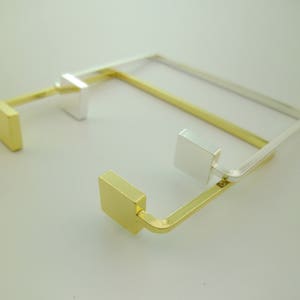 Puede incluir: Un brazalete de oro y plata con un diseño cuadrado. El brazalete está hecho de dos piezas de metal que se unen en los extremos.