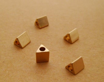 May include: Five gold triangle-shaped beads with a hole in the center. The beads are arranged in a semi-circle on a brown surface.