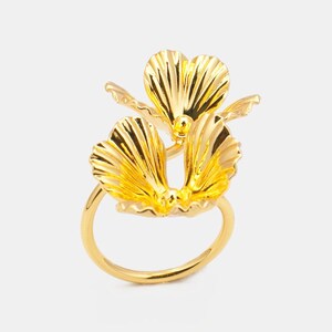 Könnte beinhalten: Ein goldener Ring mit einem Blumendesign. Die Blume besteht aus zwei sich überlappenden Blütenblättern, die jeweils eine strukturierte Oberfläche haben.
