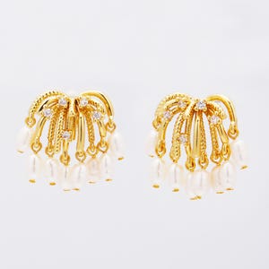 Puede incluir: Un par de pendientes dorados con un diseño en forma de abanico. Cada pendiente presenta pequeñas perlas colgantes y detalles brillantes. Los pendientes tienen una apariencia texturizada y ornamentada, adecuada para ocasiones formales.