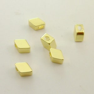 May include: Six gold-colored metal beads with a diamond shape and a hole in the center. The beads are scattered on a white surface.