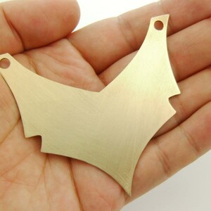 May include: A gold-coloured metal pendant shaped like a V with two holes at the top. The pendant has a brushed finish.