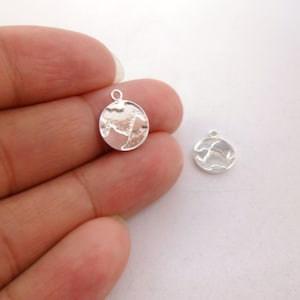 Puede incluir: Dos abalorios de metal plateados en forma de Tierra. Los abalorios tienen un diseño de globo detallado y un bucle para sujetarlos a joyas.