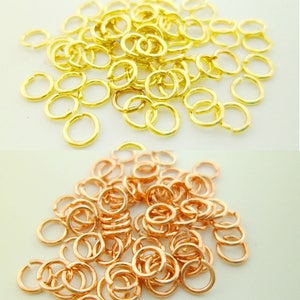 Op de afbeelding: Een stapel gouden springringen en een stapel roségouden springringen. De springringen zijn klein en rond.