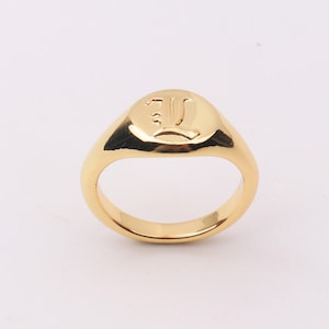 Puede incluir: Un anillo de sello de oro con una letra "L" en relieve en la parte superior.