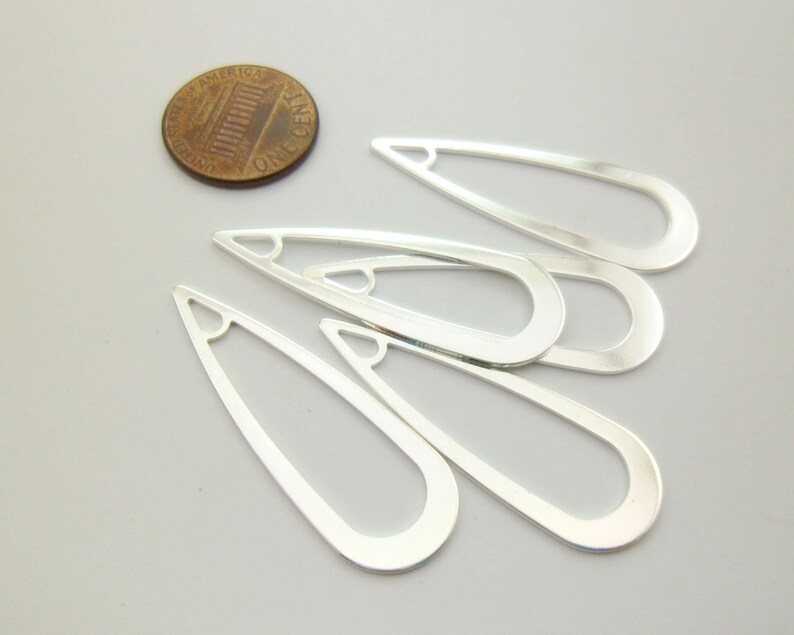 May include: Five silver-toned metal teardrop-shaped earring blanks with a hole at the top. The blanks are approximately the size of a US penny.