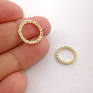 May include: Two gold-toned metal rings with clear crystal embellishments. The rings are round and have a smooth, polished finish.