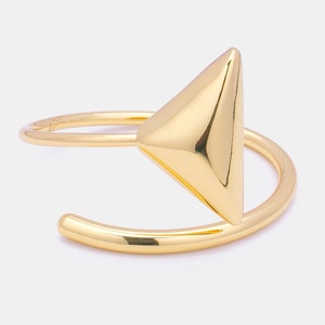 Peut inclure: Un bracelet manchette doré avec un design triangulaire géométrique. Le bracelet présente une finition polie et une esthétique minimaliste et moderne. Le triangle est le point central, ajoutant une touche audacieuse au bijou.