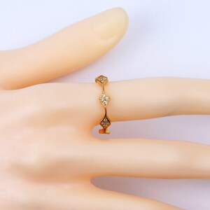 Puede incluir: Un anillo de banda de oro con una fila de cinco engastes en forma de diamante, cada uno con un racimo de peque&ntilde;os diamantes.