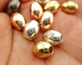 May include: A collection of oval-shaped beads in gold, silver, and rose gold tones. Some beads have a logo engraved on them.