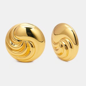 May include: A pair of gold-colored, domed earrings. Each earring features a swirling, ridged design on its surface. The earrings have a shiny, reflective finish, and are set against a plain background.