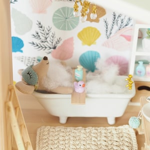 May include: A plush toy animal enjoying a bath in a white bathtub with a pink rubber duck and a bottle of bubble bath. The bathtub is surrounded by white foam and the background is a white wall with a seashell pattern.