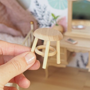 May include: A small wooden stool with a round seat and four legs. The stool is made of natural wood and has a simple design.
